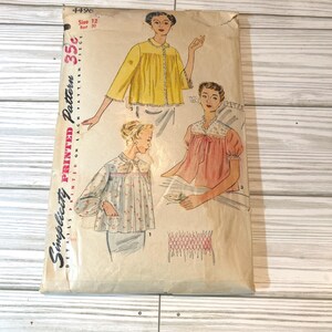 May include: Vintage Simplicity sewing pattern for a women's blouse. The pattern is for size 12 and is printed on each pattern piece. The pattern shows three different styles of blouses, all with a gathered neckline and short sleeves. The pattern is in good condition and has a light yellow background.