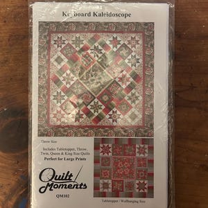 May include: A packaged quilt pattern titled "Keyboard Kaleidoscope." The pattern features a colorful patchwork design with red, green, and tan squares and star patterns. The package includes instructions for table toppers, throws, and twin, queen, and king-size quilts.