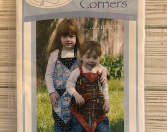 May include: A sewing pattern for a kids' apron, featuring two children wearing colorful aprons with a patchwork design. The pattern is titled "Kids' Four Corners...apron!" and is from Vanilla House Designs.