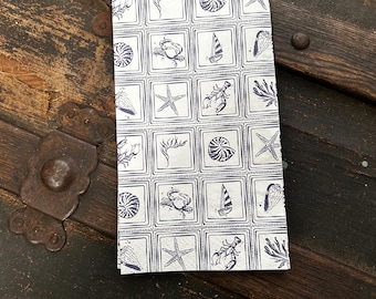 Mini nautical designs including sea shells, and a sailboat on a Guest Paper Napkin. Each design is approx 1”.  There is a minor flaw on each