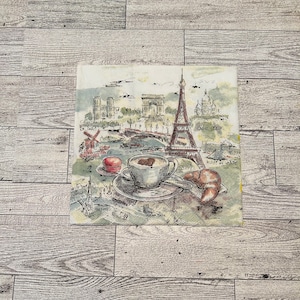 May include: A watercolor illustration of a Parisian cafe scene with a cup of coffee, a croissant, and a macaron. The Eiffel Tower, Arc de Triomphe, and other Parisian landmarks are depicted in the background.