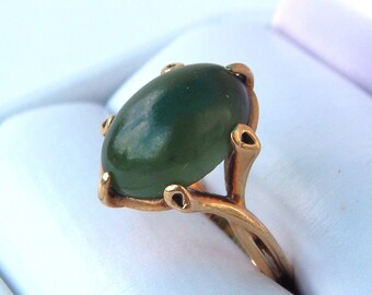 May include: A gold ring with a green oval gemstone set in a prong setting. The ring is in a white ring box.