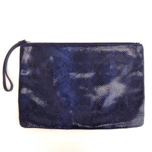 May include: A navy blue clutch with a snakeskin pattern. The rectangular bag has a zipper closure and a small wrist strap. The bag is set against a white background.