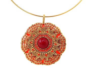 Puede incluir: Collar dorado con un colgante grande y ornamentado. El colgante presenta una piedra roja central rodeada de filigrana dorada y detalles de esmalte rojo. Se muestra sobre un fondo blanco.