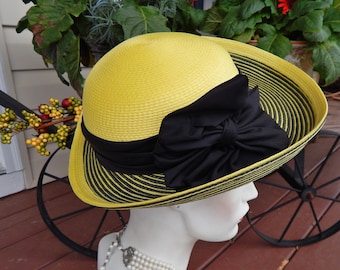 May include: A yellow and black striped straw hat with a large black bow. The hat is sitting on a mannequin's head.