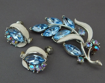 Op de afbeelding: Een vintage set met blauwe en zilverkleurige oorbellen en een broche met een bladontwerp en iriserende strasssteentjes.