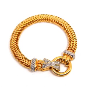 May include: A gold bracelet with a diamond-encrusted clasp. The bracelet is made of a woven chain design.