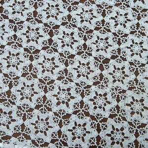 May include: Close-up of a cream-colored, crocheted lace doily. The intricate pattern features repeating floral motifs, creating a delicate and textured surface. The doily is likely handmade and adds a vintage touch.
