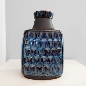 May include: A vintage ceramic vase with a dark brown neck and a rectangular body. The body is a glossy blue with a repeating geometric pattern. The vase is a decorative item.