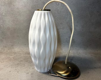 Könnte beinhalten: Eine weiße Glas-Hängeleuchte mit vertikaler Wellenstruktur. Die Lampe verfügt über eine messingfarbene Metallkappe an der Oberseite und eine passende runde Deckenhalterung, die durch ein weißes Stromkabel verbunden sind.