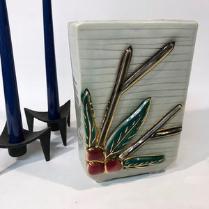 Könnte beinhalten: Eine weiße Keramikvase mit strukturierter Oberfläche und einem erhabenen Blumendesign. Das Design zeigt goldene und grüne Blätter und rote Beeren.