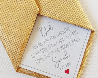 May include: A gold tie with a white card tucked inside. The card has a handwritten message that reads "Dad, Thank you for walking by my side today and always. Love you to the moon & back. Sarah 16.09.2024".
