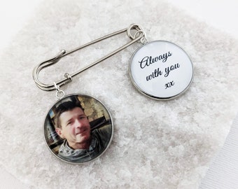 Può includere: Una spilla da balia in metallo color argento con due ciondoli circolari. Un ciondolo mostra una fotografia a colori di una persona, mentre l'altro presenta il testo stampato in nero Always with you xx su uno sfondo bianco.