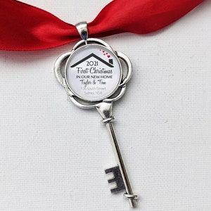 May include: A silver key-shaped Christmas ornament with a round white disc featuring the text "2021 First Christmas in our new home Taylor & Tow 106 South Street Sydney, NSW" and red hearts.