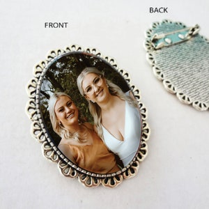 Pu&ograve; includere: Broche ovale in argento con una foto di due donne sorridenti. La broche ha un bordo decorativo a festoni. Il retro della broche ha una spilla e un design testurizzato.