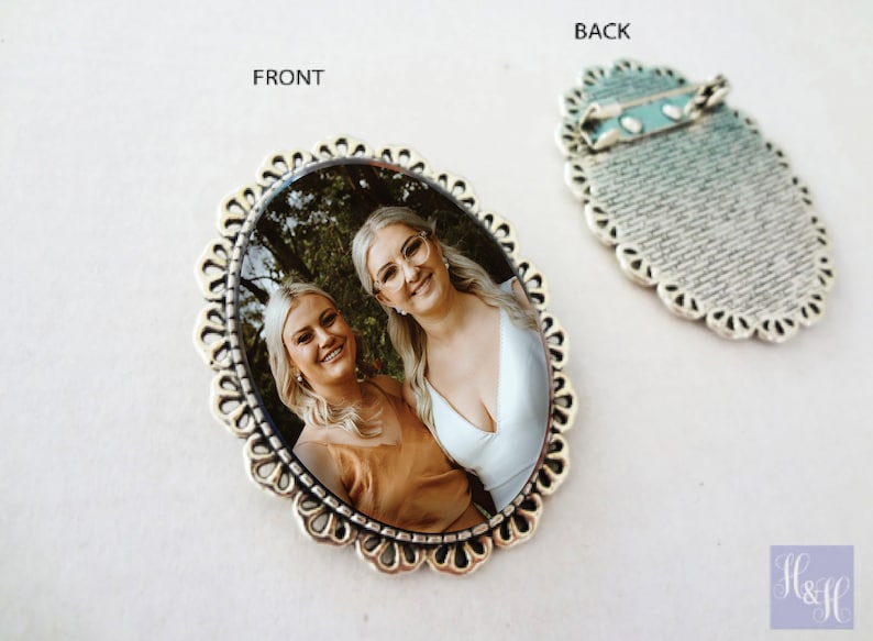 Pu&ograve; includere: Broche ovale in argento con una foto di due donne sorridenti. La broche ha un bordo decorativo a festoni. Il retro della broche ha una spilla e un design testurizzato.