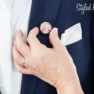 May include: A person adjusting a black button with a photo inside on a navy blue suit jacket. The jacket has a white pocket square. The text "Styled by you" is visible in the upper right corner of the image.
