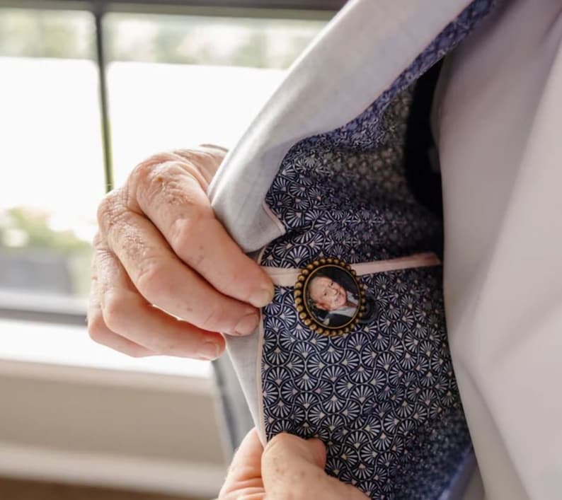 May include: A light blue blazer with a white and blue patterned lining. A small round pin with a photo of a man is attached to the lining.