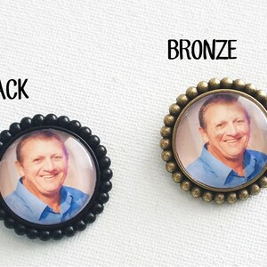 May include: Two round photo memorial pins, one with a black frame and one with a bronze frame. Both pins feature a photo of a man smiling.