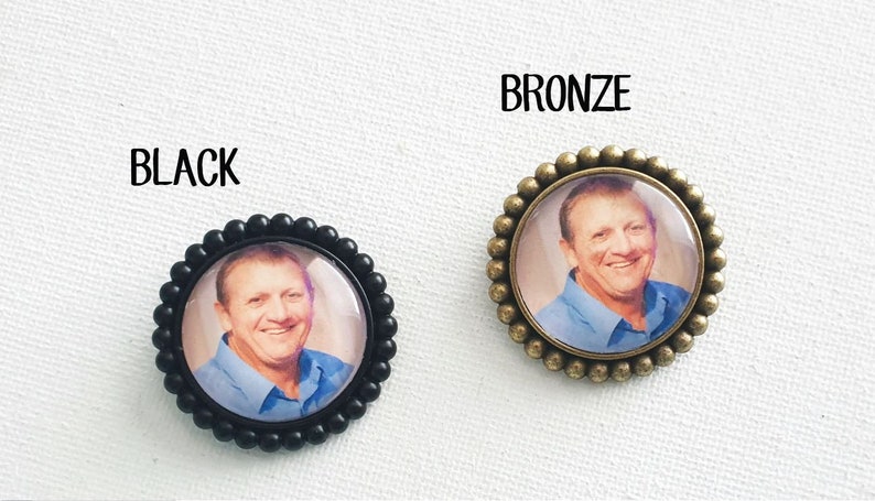 May include: Two round photo memorial pins, one with a black frame and one with a bronze frame. Both pins feature a photo of a man smiling.