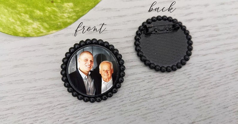 May include: Black and white photo of two men in a round, black, beaded frame. The back of the frame has a pin for attaching it to clothing. The text "front" is written above the frame and "back" is written above the back of the frame.