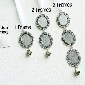 May include: Three silver picture frames with ornate designs, each with a white ribbon and a small silver heart charm. The frames are labelled "1 Frame", "2 Frames", and "3 Frames". A small white adhesive backing is also shown.