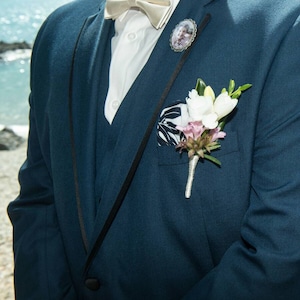 Pu&ograve; includere: Una giacca di abito blu scuro con una camicia bianca, un papillon di raso e un piccolo boutonniere floreale. Il boutonniere &egrave; sul risvolto sinistro della giacca.