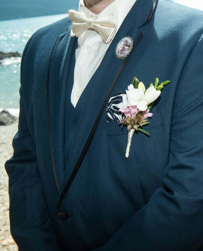 Pu&ograve; includere: Una giacca di abito blu scuro con una camicia bianca, un papillon di raso e un piccolo boutonniere floreale. Il boutonniere &egrave; sul risvolto sinistro della giacca.