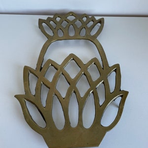 May include: A gold-toned metal trivet shaped like a pineapple. The trivet is made from a single piece of metal and has a cut-out design.