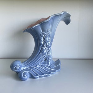 Peut inclure: Un vase en céramique bleu et rose avec un motif floral. Le vase a la forme d'une corne et une large ouverture en haut.