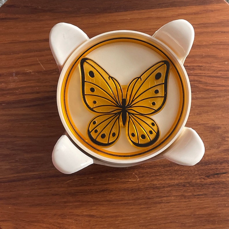 May include: A white plastic butterfly-shaped dish with a yellow butterfly design. The dish has a raised rim and a smooth surface.