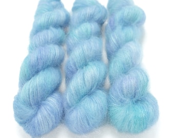 May include: Three skeins of soft, blue and turquoise yarn with a fuzzy texture. The yarn is arranged in a row, with the skeins overlapping slightly.