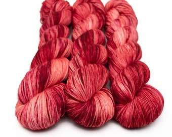 May include: Four skeins of red and pink hand-dyed yarn with a variegated color pattern.