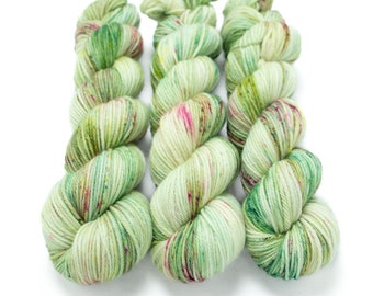 May include: Three skeins of yarn in a green, white, and pink colorway. The yarn is a fingering weight and has a speckled appearance.