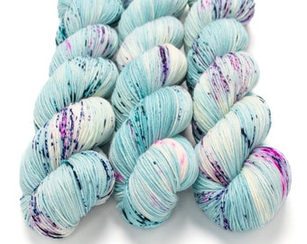 May include: Three skeins of yarn in a light blue color with white and pink speckles. The yarn is arranged in a loose braid.