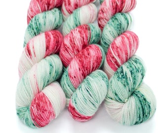 Op de afbeelding: Drie bollen garen in een rood, wit en groene kleurstelling. Het garen is een gespikkeld patroon met een subtiele glans.
