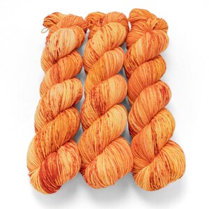 May include: Three skeins of orange and yellow variegated yarn are arranged vertically against a white background. The yarn has a textured appearance with darker orange and red streaks throughout. The yarn is tightly wound into a twisted shape.