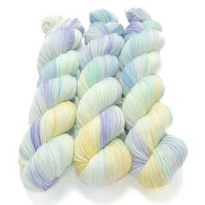 May include: Three skeins of yarn in a light blue, yellow, and purple colorway. The yarn is arranged in a spiral pattern.