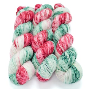 May include: Three skeins of yarn in a red, white and green colourway. The yarn is a speckled pattern with a subtle shimmer.