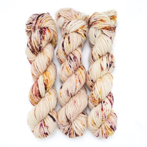 May include: Three skeins of yarn in a cream colour with flecks of burgundy, orange, and yellow.