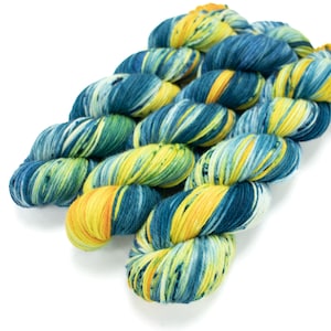 Op de afbeelding: Drie bollen garen in een blauwe, groene en gele kleurstelling. Het garen is handgeverfd en heeft een gespikkeld uiterlijk.