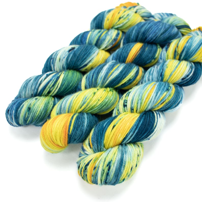 Op de afbeelding: Drie bollen garen in een blauwe, groene en gele kleurstelling. Het garen is handgeverfd en heeft een gespikkeld uiterlijk.