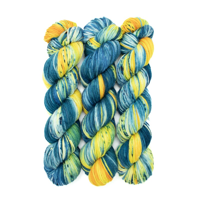 Op de afbeelding: Drie bollen garen in een blauwe, gele en groene kleurstelling. Het garen is handgeverfd en heeft een gespikkeld uiterlijk.