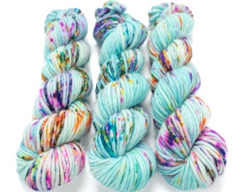 May include: Three skeins of yarn in a light blue color with a multi-colored speckled pattern. The yarn is arranged in a row, with the skeins overlapping.