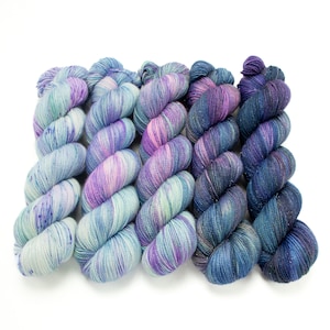 May include: Five skeins of yarn in a gradient of blue, purple and green colours. The yarn is a fingering weight and has a subtle sparkle.