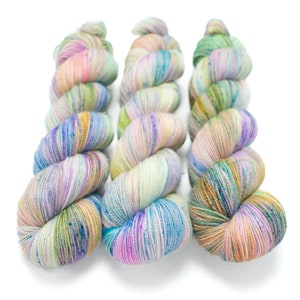 May include: Three skeins of colorful yarn with a speckled, variegated pattern in shades of blue, green, pink, and yellow. The yarn is wound into a loose coil.