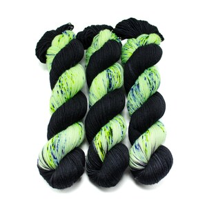 May include: Three skeins of yarn in a black and green colourway. The yarn is a speckled green with black flecks and black yarn with green flecks.