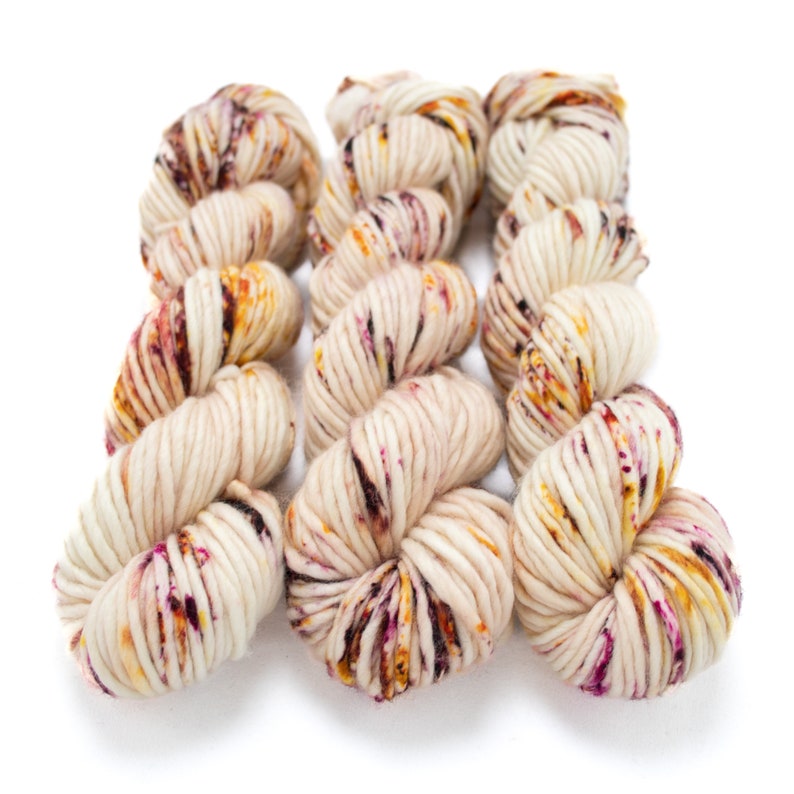 May include: Six skeins of yarn in a cream colour with flecks of pink, orange, and brown.
