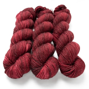 May include: Several skeins of burgundy-colored yarn with subtle flecks of silver. The yarn is arranged in a neat row, showcasing its texture and color variations. Ideal for knitting or crocheting projects.