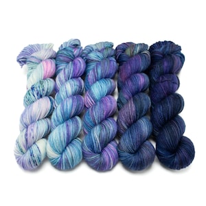 May include: Five skeins of yarn in a gradient of blue and purple colors. The yarn is hand-dyed and has a speckled effect.